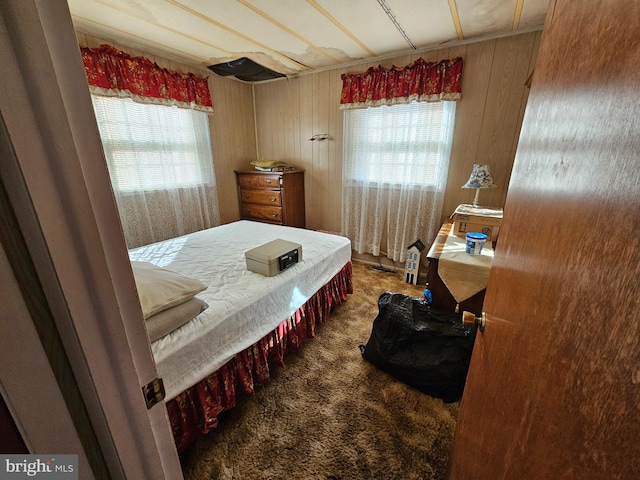 carpeted bedroom featuring multiple windows and wooden walls