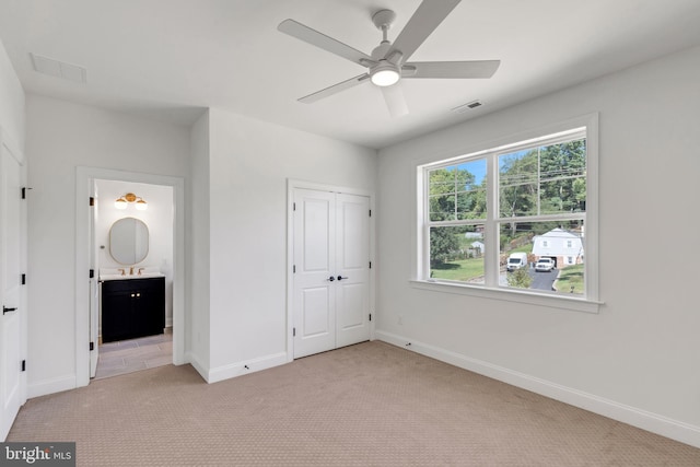 unfurnished bedroom with ceiling fan, connected bathroom, light colored carpet, and a closet