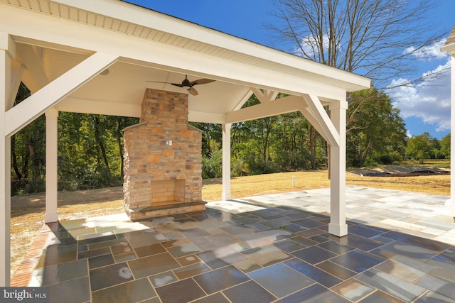 view of terrace featuring an outdoor stone fireplace, ceiling fan, and a gazebo