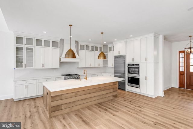 kitchen with appliances with stainless steel finishes, white cabinetry, light hardwood / wood-style floors, and decorative light fixtures