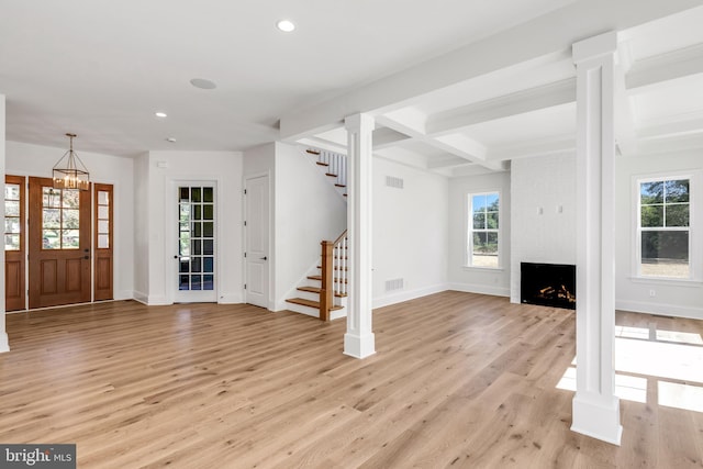 unfurnished living room featuring a chandelier, decorative columns, a fireplace, beam ceiling, and light wood-type flooring