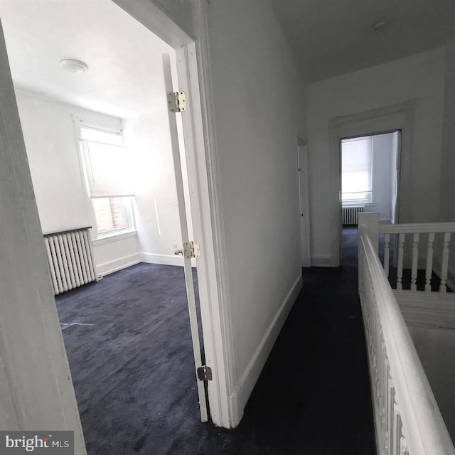 corridor featuring radiator, a wealth of natural light, and dark carpet