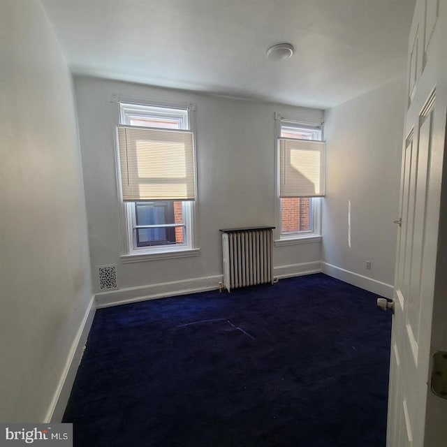 spare room with radiator and dark carpet