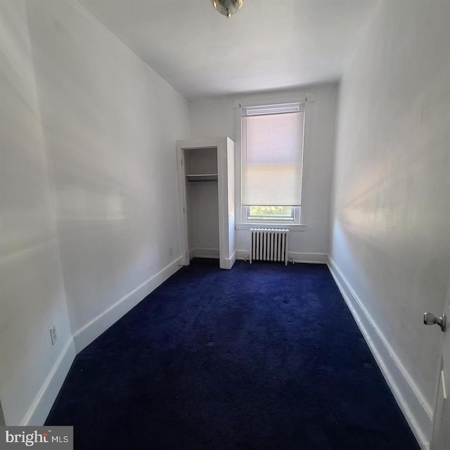 unfurnished bedroom featuring dark colored carpet, a closet, baseboards, and radiator heating unit