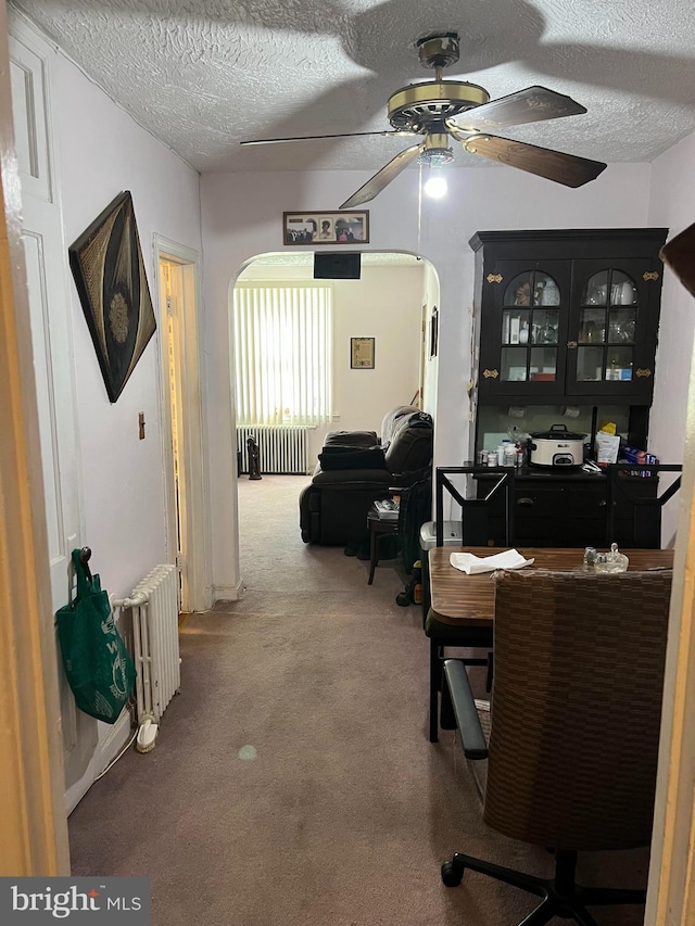 carpeted office space with radiator heating unit, ceiling fan, and a textured ceiling