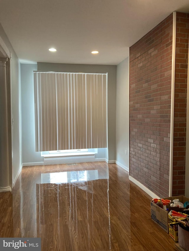 spare room featuring brick wall and dark hardwood / wood-style floors