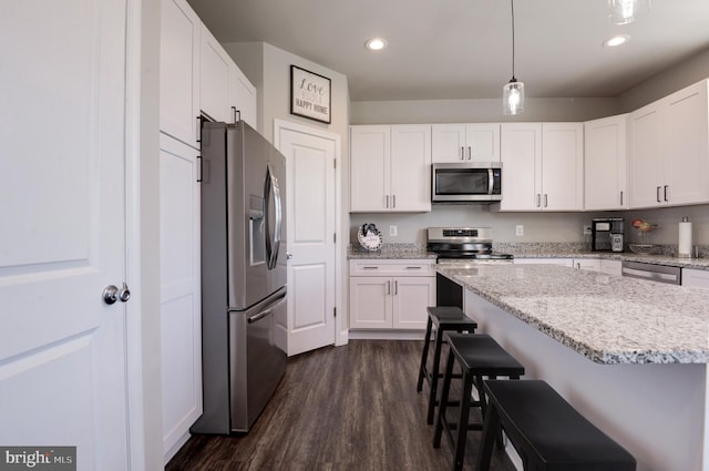 kitchen featuring appliances with stainless steel finishes, a kitchen breakfast bar, pendant lighting, dark hardwood / wood-style floors, and white cabinetry