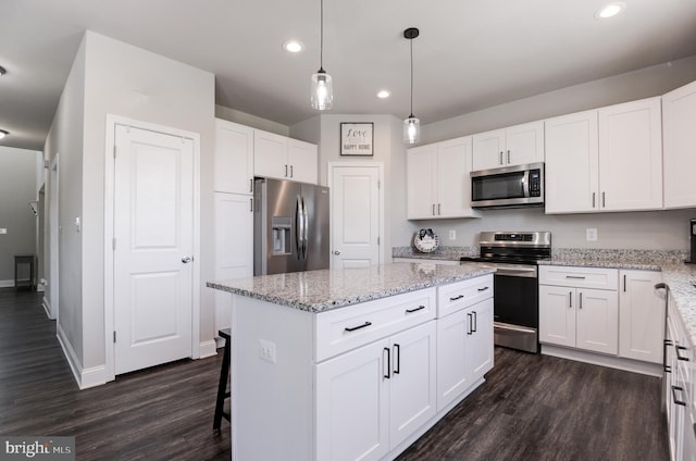 kitchen with white cabinets, dark hardwood / wood-style floors, appliances with stainless steel finishes, decorative light fixtures, and a kitchen island