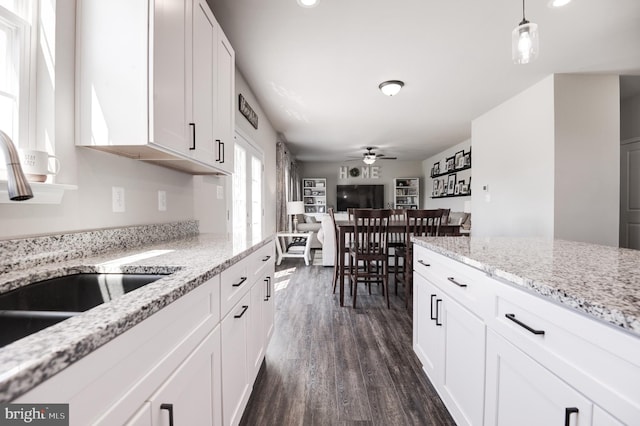 kitchen with dark wood-type flooring, white cabinets, ceiling fan, decorative light fixtures, and light stone counters