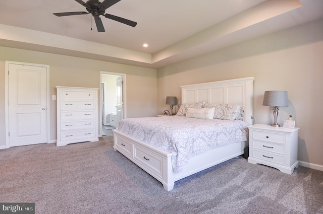 bedroom featuring carpet floors, a tray ceiling, ensuite bath, and ceiling fan