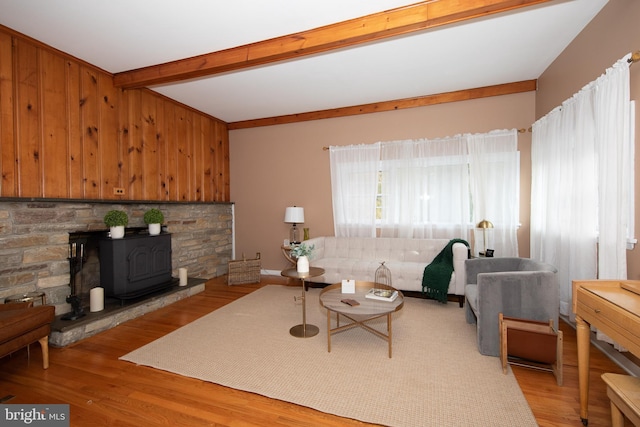 living room with a fireplace, a wood stove, light wood-type flooring, and beamed ceiling