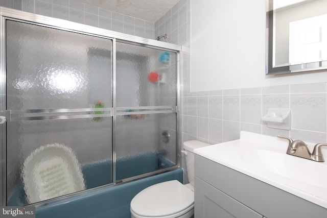 full bathroom with vanity, tile walls, bath / shower combo with glass door, toilet, and tasteful backsplash