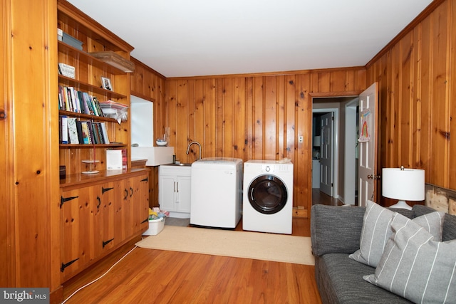 washroom with washer and dryer, wood walls, light hardwood / wood-style flooring, and cabinets