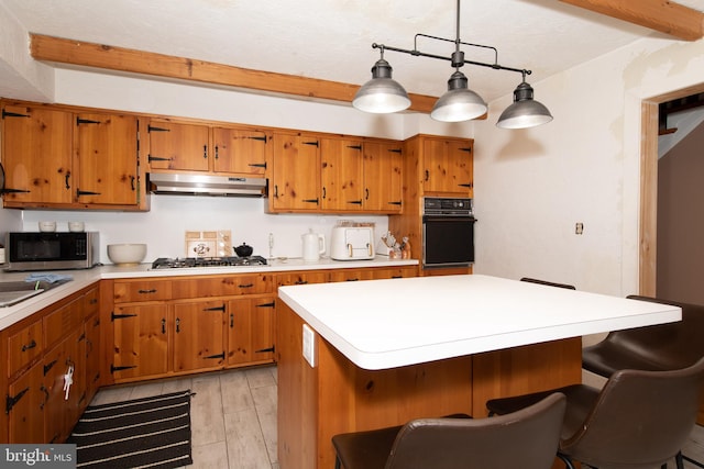 kitchen with appliances with stainless steel finishes, hanging light fixtures, a kitchen island, beam ceiling, and light hardwood / wood-style flooring