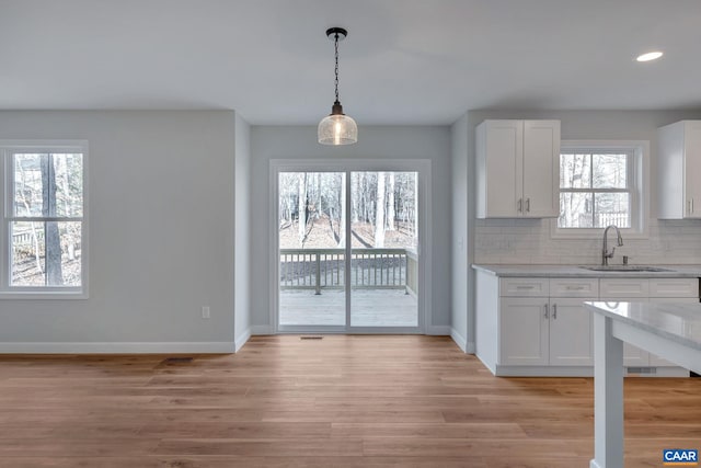 kitchen featuring white cabinets, light hardwood / wood-style flooring, hanging light fixtures, and tasteful backsplash