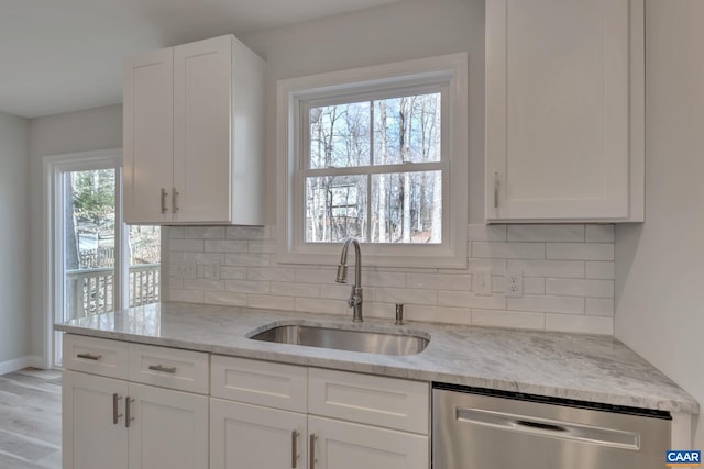 kitchen with sink, white cabinets, stainless steel dishwasher, light stone countertops, and light wood-type flooring