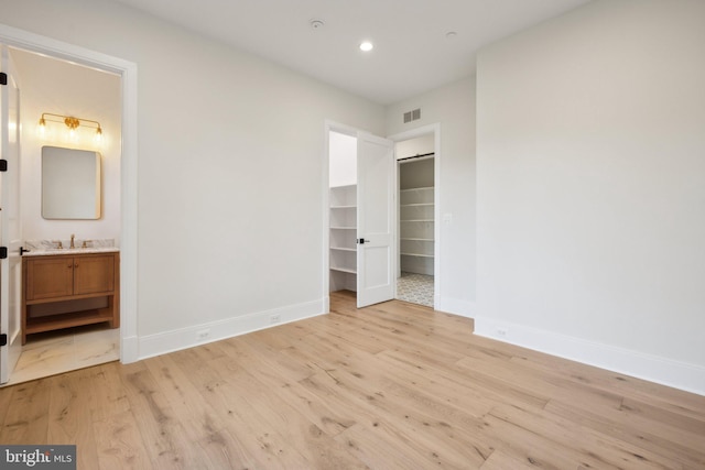 unfurnished bedroom with connected bathroom, sink, a spacious closet, and light wood-type flooring