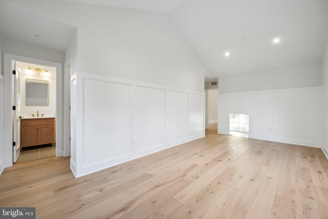 additional living space with sink, high vaulted ceiling, and light hardwood / wood-style flooring