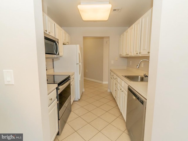 kitchen with appliances with stainless steel finishes, sink, light tile flooring, and white cabinets