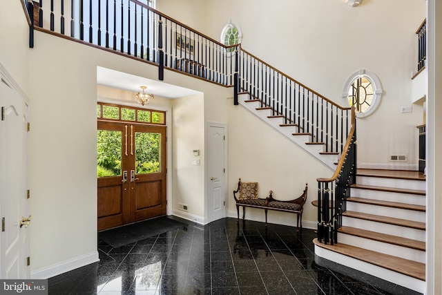 foyer entrance featuring a chandelier, dark tile floors, a towering ceiling, and french doors