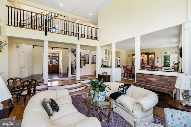 living room featuring a towering ceiling, dark wood-type flooring, and decorative columns