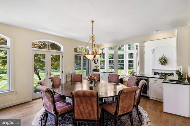 dining area featuring a fireplace, sink, light hardwood / wood-style flooring, a chandelier, and french doors