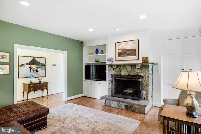 living room with built in features, a fireplace, and light hardwood / wood-style flooring