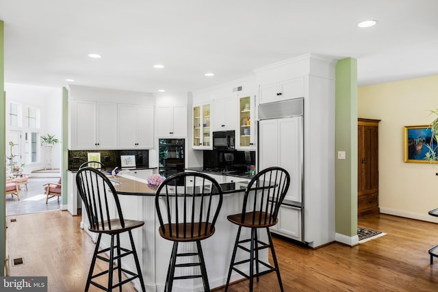 kitchen with a kitchen breakfast bar, black appliances, white cabinetry, backsplash, and light wood-type flooring