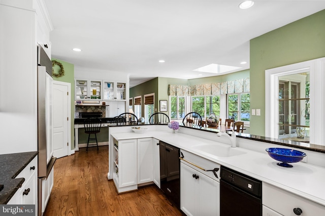 kitchen with a skylight, black dishwasher, a stone fireplace, white cabinetry, and dark hardwood / wood-style floors