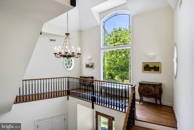 stairway with an inviting chandelier, a wealth of natural light, hardwood / wood-style floors, and a towering ceiling