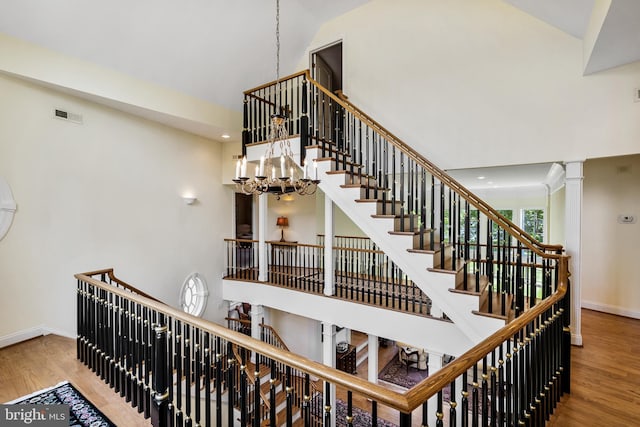 staircase featuring a notable chandelier, decorative columns, high vaulted ceiling, and light wood-type flooring