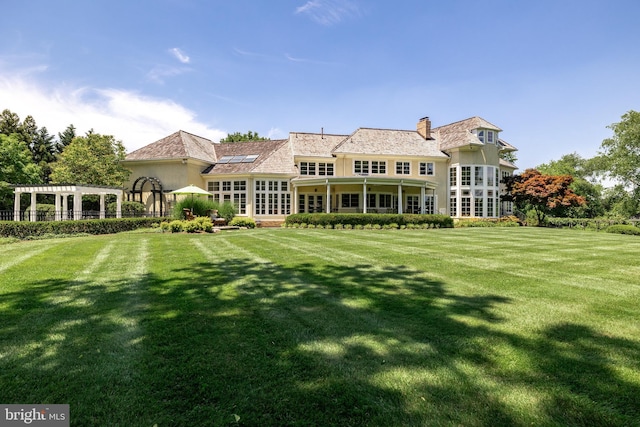 back of property with a pergola and a lawn