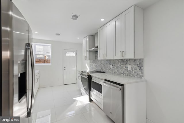 kitchen with light tile flooring, wall chimney range hood, stainless steel appliances, white cabinetry, and light stone countertops