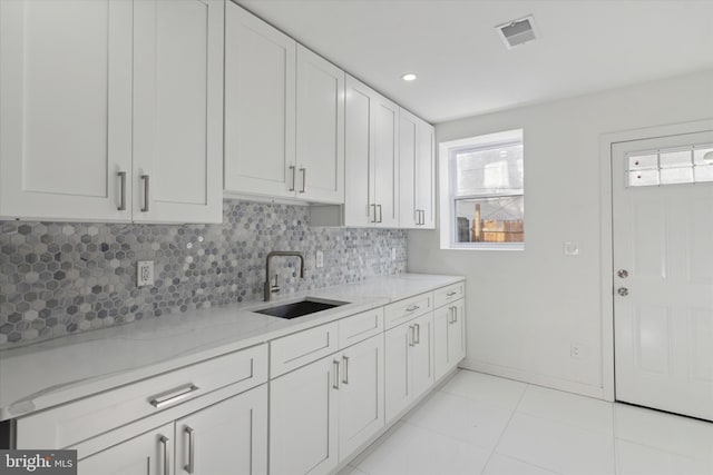 kitchen featuring light tile floors, tasteful backsplash, white cabinetry, sink, and light stone counters