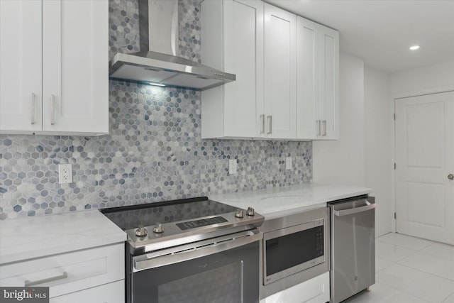 kitchen featuring wall chimney range hood, light stone countertops, white cabinetry, appliances with stainless steel finishes, and backsplash