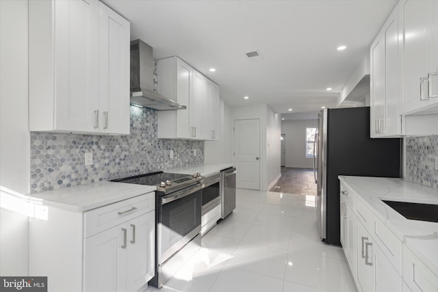 kitchen with wall chimney range hood, stainless steel appliances, backsplash, light hardwood / wood-style floors, and white cabinets