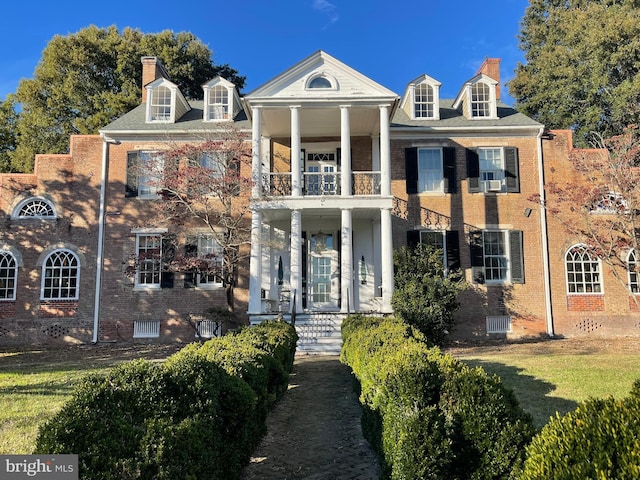 greek revival house featuring a front yard, a porch, central AC unit, and a balcony