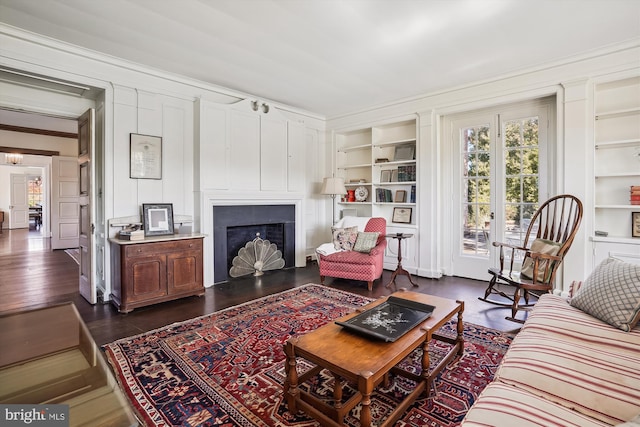 living room featuring built in shelves, ornamental molding, and dark wood-type flooring