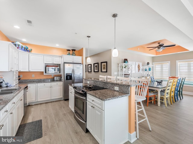 kitchen with appliances with stainless steel finishes, ceiling fan, a breakfast bar area, light hardwood / wood-style floors, and white cabinets