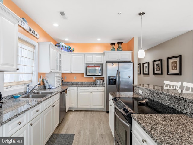 kitchen with appliances with stainless steel finishes, pendant lighting, light wood-type flooring, and white cabinetry