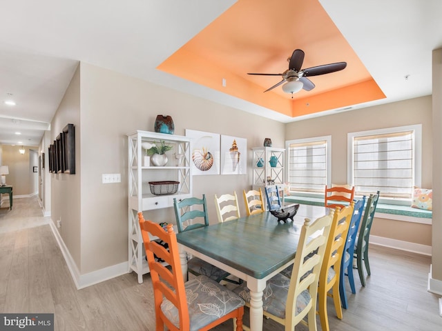 dining area with ceiling fan, a raised ceiling, and light hardwood / wood-style flooring