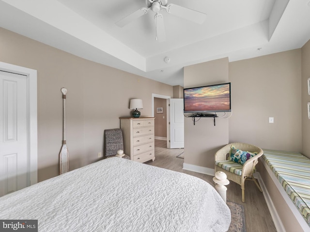 bedroom with ceiling fan, light wood-type flooring, and a tray ceiling