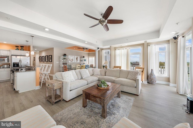 living room featuring ceiling fan, light wood-type flooring, and a tray ceiling