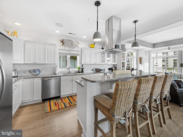 kitchen with stainless steel appliances, a kitchen breakfast bar, hanging light fixtures, island exhaust hood, and sink