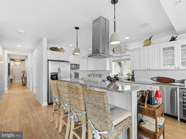 kitchen with appliances with stainless steel finishes, stone counters, island exhaust hood, and white cabinetry