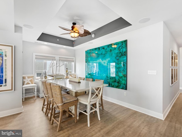 dining area featuring a tray ceiling, ceiling fan, and light hardwood / wood-style flooring