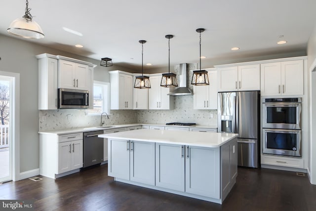 kitchen featuring a sink, wall chimney range hood, a center island, stainless steel appliances, and light countertops