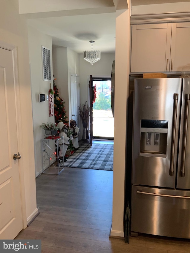 kitchen with pendant lighting, white cabinets, wood-type flooring, an inviting chandelier, and stainless steel refrigerator with ice dispenser