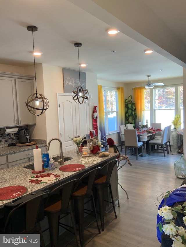 kitchen featuring light stone countertops, light hardwood / wood-style floors, decorative light fixtures, and a breakfast bar area