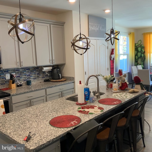 kitchen featuring light stone countertops, light wood-type flooring, an island with sink, and decorative light fixtures